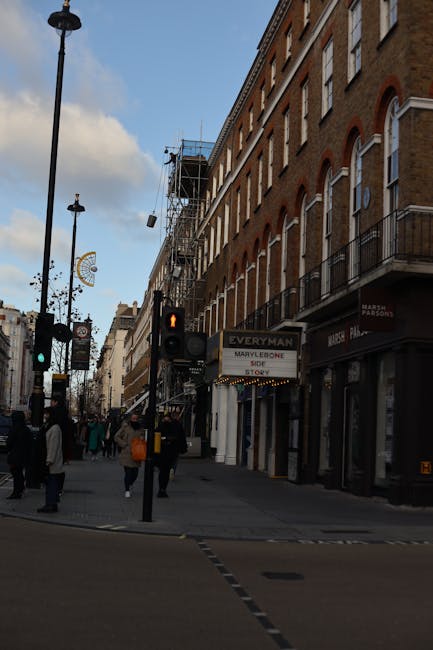 Photograph of the storefront of The Marylebone pub, located on a high street with orange brick buildings. The pub's exterior features a large, vintage-style sign with the name 'The Marylebone' and add